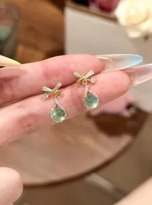 Close-up of elegant bowknot earrings with green waterdrop stones and sparkling zircons
