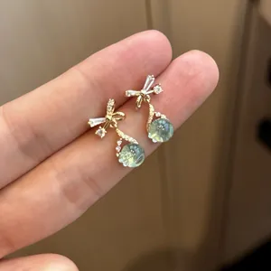 Detail shot of elegant gold bow earrings with dangling green teardrop zircon stones.