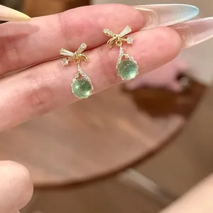 Macro detail of elegant bowknot earrings featuring light green teardrop zircon pendants