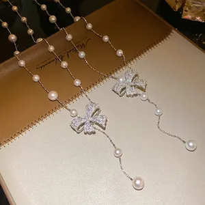 Detailed view of two sparkling zircon bowknot pendants with delicate pearl bead necklaces