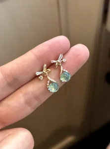 Macro view of gold bow earrings with green drop pendants and sparkling zircons