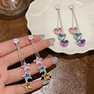 Macro view of colorful heart and star zircon tassel earrings resting on white ceramic plate.