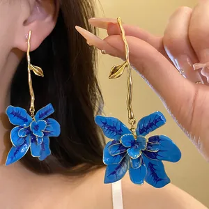Dettaglio di orecchini a fiore in smalto blu con design a ramo color oro elegante.
