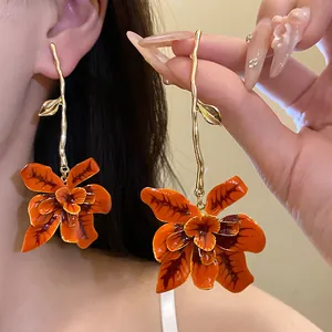 Dettaglio di orecchini a goccia vintage con fiore in smalto arancione e ramo d'oro