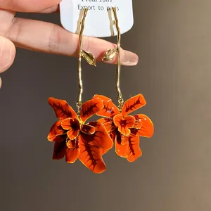 Primo piano di orecchini pendenti vintage con fiori in smalto arancione e rami dorati.