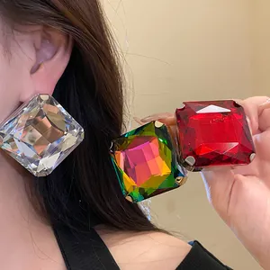 Close-up of oversized square crystal stud earrings in clear, iridescent, and red