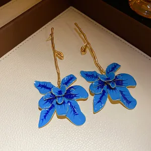 Dettaglio di orecchini a fiore in smalto blu artistico con steli dorati a ramo