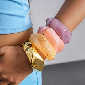 Macro view of colorful irregular resin and gold metal geometric bangles worn on arm