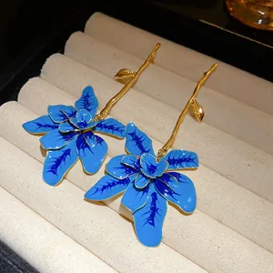 Dettaglio di orecchini a fiore in smalto blu con steli dorati in un portagioie.