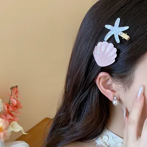 Detailed view of resin starfish and pink seashell hair clips worn on dark wavy hair