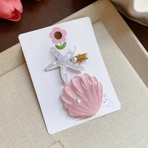 Detailed close-up of pink shell and white starfish resin hair clips on display card