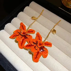Dettaglio di orecchini a fiore arancione smaltato con lunghi steli dorati a ramoscello