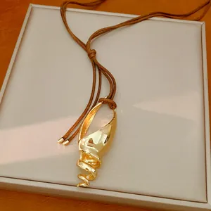 Dettaglio di una collana con ciondolo a conchiglia dorata e cordino in pelle marrone.