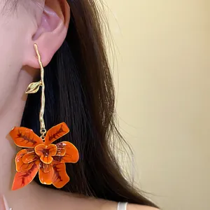 Vista dettagliata di eleganti orecchini pendenti a fiore in smalto arancione su modella