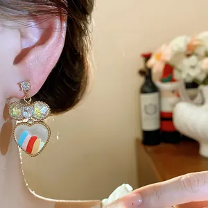 Gros plan d'une boucle d'oreille cœur plaquée or 18 carats avec rayures arc-en-ciel et nœud