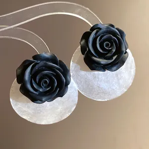 Dettaglio di orecchini a perno con rosa in resina nera e dischi di conchiglia lucidi