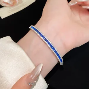 Close-up view of a luxury bangle with blue sapphire-colored zircons worn on a wrist.