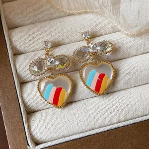 Gros plan de boucles d'oreilles cœur en or 18k avec rayures colorées et cristaux