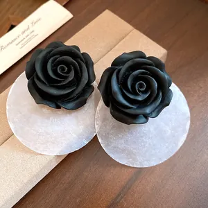 Dettaglio di orecchini eleganti a rosa in resina nera con un disco di conchiglia