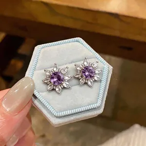 Elegant purple zircon flower clip-on earrings displayed on a light blue velvet jewelry box.