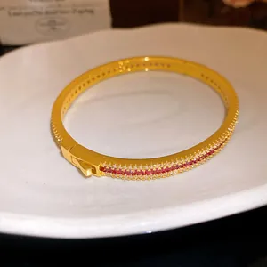 Detail of gold-plated bangle with red and white zircon stones on white plate