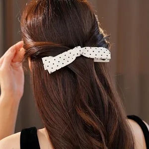 Elegant minimalist white polka dot bow hair clip accessory shown on long wavy brown hair