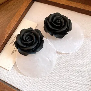 Primo piano di orecchini a rosa in resina nera con dischi di conchiglia bianca traslucida.