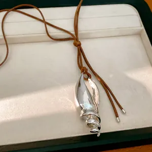 Dettaglio ravvicinato di un ciondolo a conchiglia metallica su collana in cuoio.
