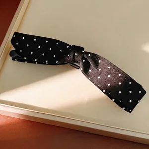 Elegant black polka dot bow hair clip with fabric texture presented on a minimal display tray