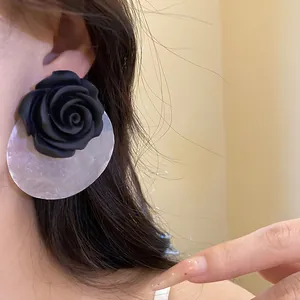 Primo piano dettagliato degli orecchini con rosa in resina nera e conchiglia indossati
