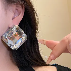 Close-up detail of oversized faceted square crystal ear studs with silver needle base