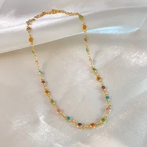 Macro detail of colorful resin bead necklace on gold chain with shimmering white silk background