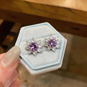 Detailed close-up of elegant purple zircon flower clip earrings in a light blue velvet gift box