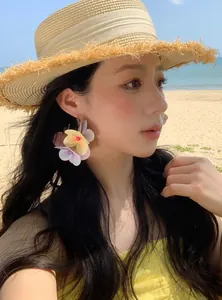 Close-up of vibrant colorful floral C-shaped earrings worn by a model at a sunny beach