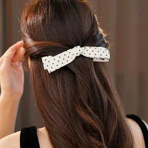 Detailed view of elegant white polka dot bow hair clip on model's dark wavy hair