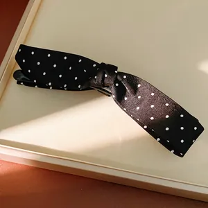 Close-up view of a black and white polka dot fabric bow hair clip with elegant luxury texture