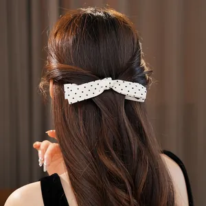 Detail shot of a white polka-dot bow hair clip styled on elegant long wavy brown hair