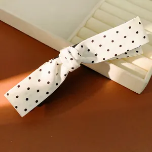 Close-up of elegant white fabric hair clip with black polka dot bow design