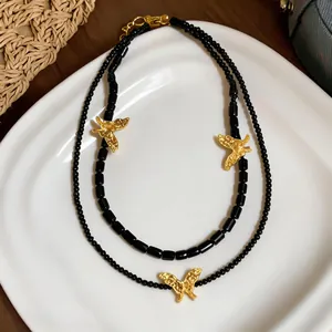 Detail of double-layer black beaded necklace with textured gold butterfly pendants.