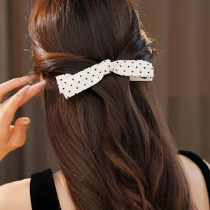 Detail showing a white polka dot bow hair clip worn on elegant brown hair.