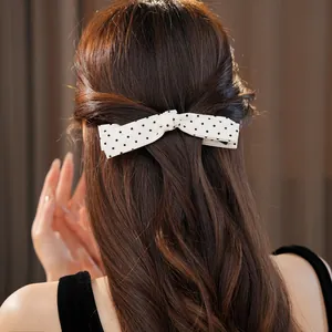 Detailed view of an elegant white polka dot bow hair clip styled on long wavy hair