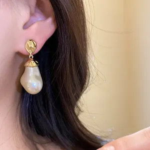 Detail shot of elegant baroque pearl drop earrings featuring hammered gold studs on a model