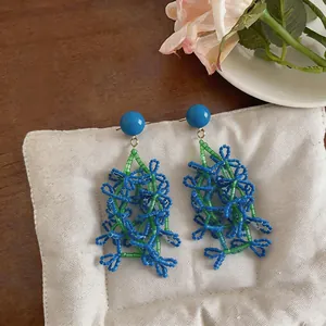 Detail view of handmade blue and green beaded tassel earrings on a soft fabric pad