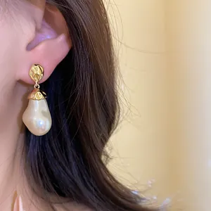 Close-up of vintage baroque pearl pendant earrings with gold pleated metal studs.