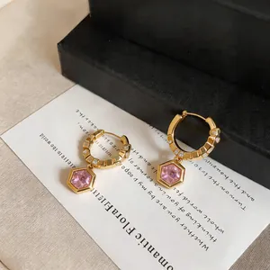 Detailed view of gold geometric hoop earrings with pink zircon pendant