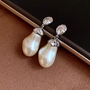 Macro view of vintage silver earrings with a large cream baroque pearl and wrinkled metallic detail
