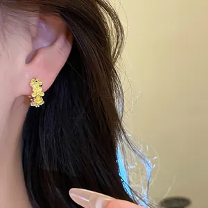Close-up detailed view of yellow drip oil flower hoop earrings worn on a female ear