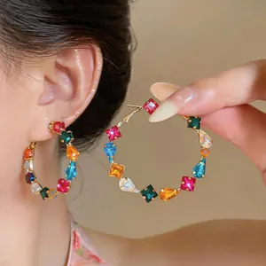 Close-up of gold hoop earrings featuring colorful square and teardrop-shaped zirconia