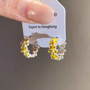 Close-up macro detail of silver hoop earrings featuring dainty yellow floral enamel design