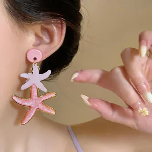 Detalle de pendientes de estrella de mar de resina rosa con borde dorado para playa.